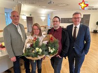 Die genannten Personen stehen im Ratssaal und schauen in die Kamera. Die Geehrten halten jeweils einen Blumenstrauß in den Händen.