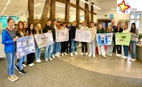 Schülerinnen und Schüler stehen nebeneinander in der Stadtbibliothek und halten ihre selbstgemachten Plakate zum thema Klimaschutz.