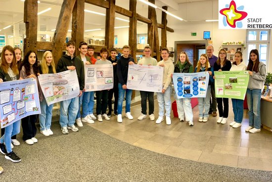 Schülerinnen und Schüler stehen nebeneinander in der Stadtbibliothek und halten ihre selbstgemachten Plakate zum thema Klimaschutz.