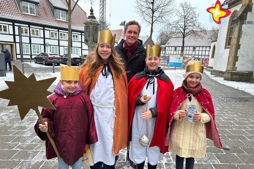 Die genannten Mädchen sind als Heilige Drei Könige verkleidet. Ein Mädchen hält einen Stern in der Hand. Alle schauen in die Kamera.