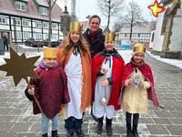 Die genannten Mädchen sind als Heilige Drei Könige verkleidet. Ein Mädchen hält einen Stern in der Hand. Alle schauen in die Kamera.