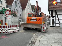 Blick auf die Baustelle in der Rathausstraße. Ein Bagger und Sperrschilder sind zu sehen.