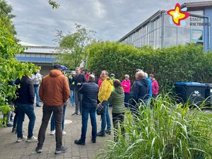 Mehre Menschen stehen als Gruppe auf einem Schulhof.