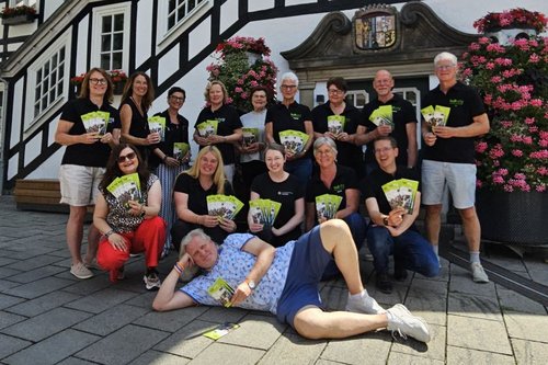 kulturig-Vertreter und Partner vor dem Rathaus. Sie zeigen das neue Programmheft in die Kamera. Michael Beckhoff, Initiator des Cultura Rock Festivals, liegt quer vor seinen Mitstreitern auf dem Boden.