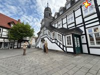 Das Bild zeigt das Rietberger Rathaus von der Seite. Davor stehen Alltagsmenschen-Skulpturen. Links blüht eine Kastanie.