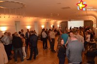 Menschen stehen im Ratssaal und schauen auf die Ergebnisse, die im hinteren Teil des Saals präsentiert werden.