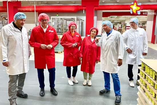 Oliver Lahode, Andreas Sunder, Anna Niehaus, Renate Pörtner, Miles Keeley und Thomas Hollensteiner stehen in rote und weiße Schutzkittel gekleidet und mit Haarnetzen ausgestattet im Halbkreis in einer Produktionshalle.