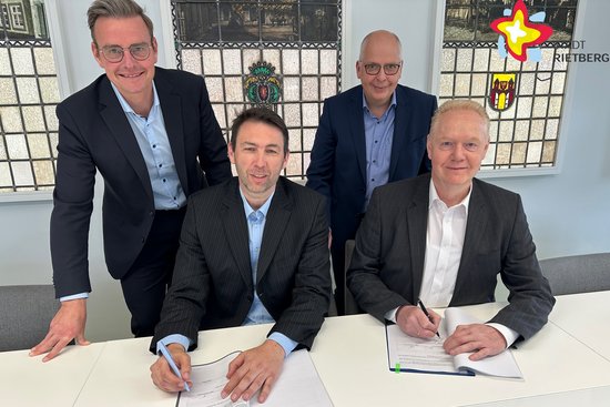 Bürgermeister Andreas Sunder, André Dreißen (Geschäftsführer Netzgesellschaft Ostwestfalen), Matthias Setter (Fachbereichsleiter Bauen Stadt Rietberg) und Dr. Thomas Vollert (Geschäftsführer Helinet-GmbH) sitzen bzw. stehen an einem Tisch. Vor ihnen liegen Unterlagen zur Unterschrift.