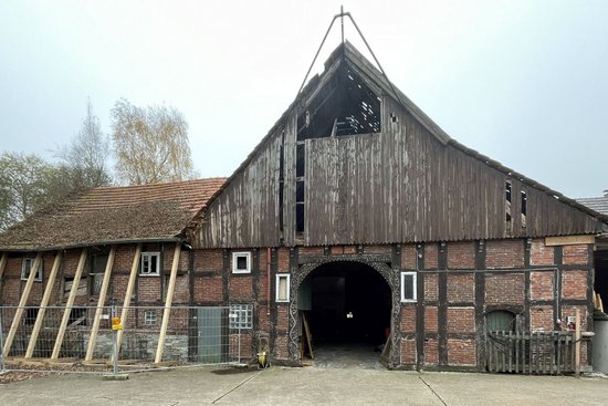 Zu sehen ist die Fachwerkfassade einer heruntergekommenen Scheune, teilweise eingezäunt.