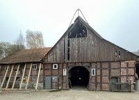 Zu sehen ist die Fachwerkfassade einer heruntergekommenen Scheune, teilweise eingezäunt.