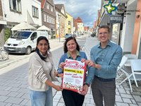Die drei genannten Personen stehen in der Rietberger Rathausstraße und halten ein Plakat hoch. Sie schauen in die Kamera.