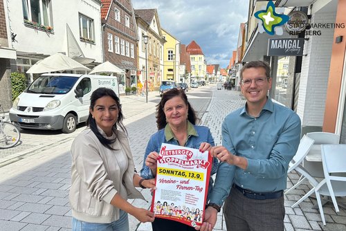 Die drei genannten Personen stehen in der Rietberger Rathausstraße und halten ein Plakat hoch. Sie schauen in die Kamera.