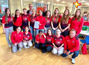 Eine Mannschaft Junioren-Fußballerinnen in roten Jacken stehen und knieen neben- und hintereineinander.