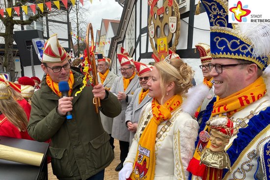 Bürgermeister Andreas Sunder reicht dem Prinzenpaar mit Prinz Manuel I. Kaiser und Prinzessin Carina I. Pahlsmeyer einen symbolischen goldenen Rathausschlüssel. Sie stehen auf einer Bühne am Rathaus. Das Prinzenpaar trägt ein Ornat.