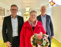 Bürgermeister Andreas Sunder und Michael Schlüter stehen links und rechts der langjährigen Mitarbeiterin Karin Schniedertöns, die zum 40-jährigen Dienstjubiläum einen Blumenstrauß erhielt, den sie in der linken Hand hält.
