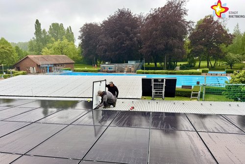 Man sieht, wie die Module installiert werden. Im Hintergrund ist das Schwimmbecken zu sehen.