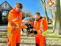 Zwei Männer in orangefarbener Arbeitskleidung reinigen mit einer Bürste einen Nistkasten.