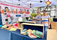 zwei Frauen stehen hinter einem Verkaufsstand mit allerhand selbstgetrickten Mützen, Handschuhen und ähnlichem.