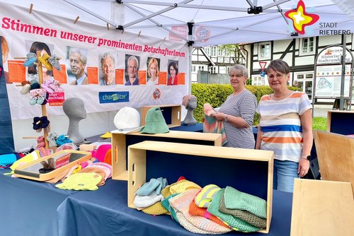 zwei Frauen stehen hinter einem Verkaufsstand mit allerhand selbstgetrickten Mützen, Handschuhen und ähnlichem.