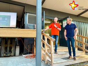 Andreas Sunder und Michael Petermeier stehen auf einer niedrigen Treppe und schauen auf einen Monitor.