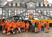 17 Männer in orangefarbener Arbeitskleisung und mit Besen und Laubbläsern in der Hand stehen zusammen mit Bürgermeister Andreas Sunder vor einem Radlader mit reichlich Mülltüten in der Schaufel.