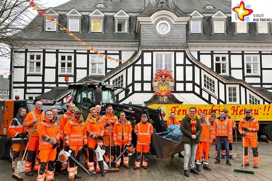 17 Männer in orangefarbener Arbeitskleisung und mit Besen und Laubbläsern in der Hand stehen zusammen mit Bürgermeister Andreas Sunder vor einem Radlader mit reichlich Mülltüten in der Schaufel.