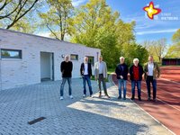 Die genannten Personen stehen vor dem neuen (eingeschossigen) Multifunktionsgebäude und schauen in die Kamera. Das Gebäude ist hell verklinkert.