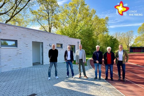 Die genannten Personen stehen vor dem neuen (eingeschossigen) Multifunktionsgebäude und schauen in die Kamera. Das Gebäude ist hell verklinkert.