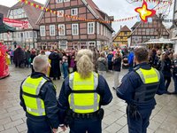 Drei uniformierte Personen blicken auf eine feiernde Menge auf der Straße. Auf ihren gelben Westen lässt sich "Ordnungsamt" lesen.