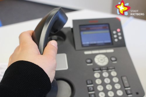 Eine Hand hebt einen Telefonhörer von einem Telefongerät.