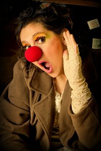 Eine geschminkte Frau mit roter Clownsnase schaut mit offenem Mund und erstauntem Blick in die Kamera.