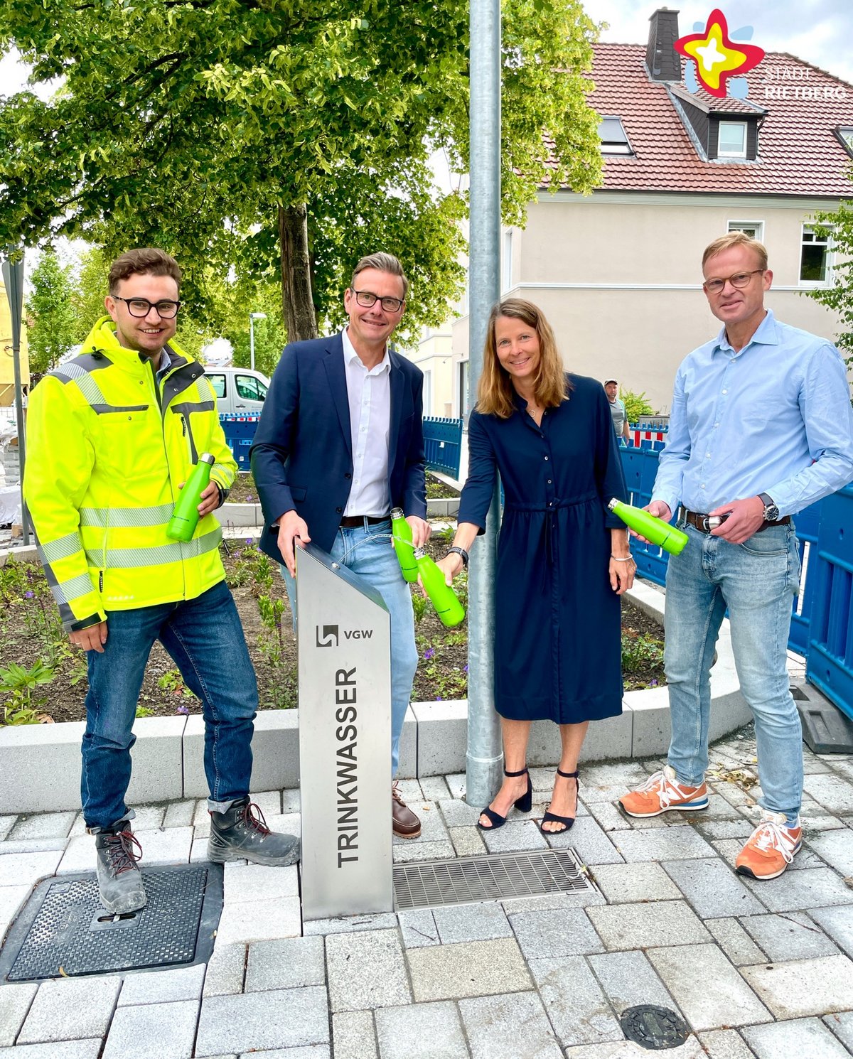 Jan Stephan, Bürgermeister Andreas Sunder, Dr. Gesa Kutschera und Dr. Carsten Behlert stehen hinter einem Trinkwasserspender an einem Radweg. Jeder hält eine grüne Flasche in der Hand, die sie mit Wasser füllen.